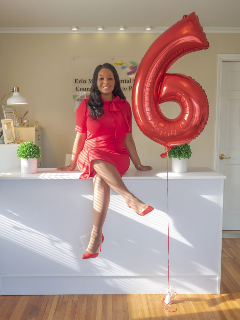 Erin sitting on front desk next to 6th anniversary balloon