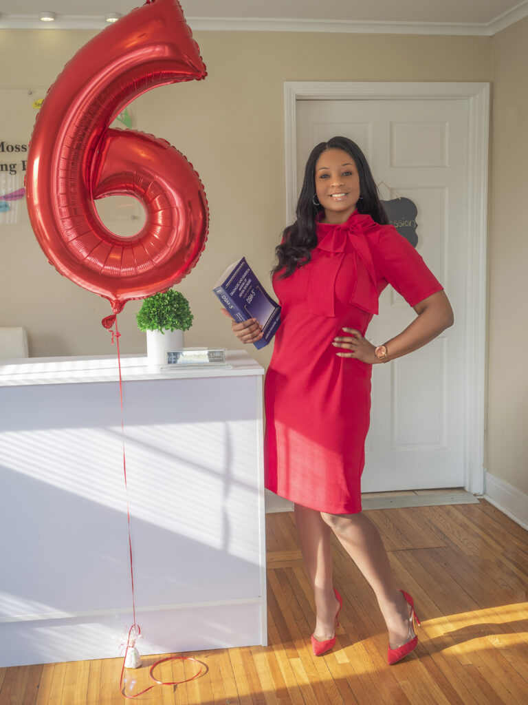 Erin M. Moss holding text book, standing next to 6th anniversary balloon