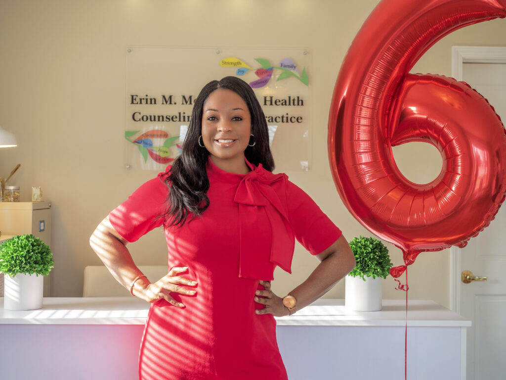 Erin M. Moss standing in front of front desk next to 6th anniversary balloon